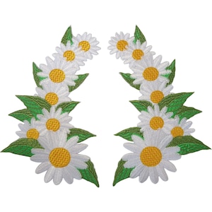 May include: Two symmetrical embroidered patches featuring a curved arrangement of white daisy flowers with bright yellow centres and green leaves. The floral design is detailed with white thread petals and textured yellow centres on a white background.
