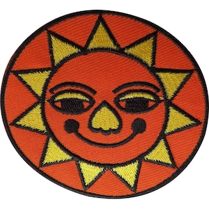 Op de afbeelding: Een ronde geborduurde patch met een gestileerde zon met een feloranje gezicht, gele driehoekige stralen en zwart gestikte details die de ogen, neus en een glimlach omlijnen. Het ontwerp is afgewerkt met een dikke zwarte rand.