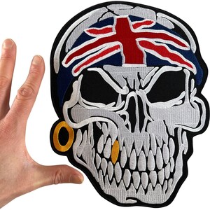May include: An embroidered patch featuring a skull wearing a bandana with a Union Jack flag design. The skull is white with black shading, a gold hoop earring, and a single gold tooth. The patch has a thick black border and a black background.
