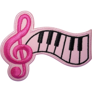 Könnte beinhalten: Ein gestickter Aufnäher mit einem leuchtend pinken Violinschlüssel, der mit einem geschwungenen Klaviertastaturabschnitt verbunden ist. Die Tastatur hat schwarze und weiße Tasten auf hellrosa Hintergrund mit einem passenden pinken Stickrand.