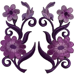 Peut inclure: Une paire d'écussons brodés symétriques présentant des motifs floraux violets. Chaque écusson affiche une grande fleur en bas et une fleur plus petite en haut, reliées par des tiges et des feuilles incurvées, le tout en fils violets.