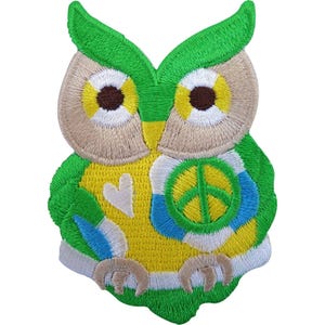 Puede incluir: Un parche bordado de búho con hilos de color verde brillante, amarillo y azul. El búho tiene ojos grandes con pupilas marrón oscuro, un corazón blanco en el pecho y un símbolo de paz amarillo y azul en el ala. Tiene patas de color canela.