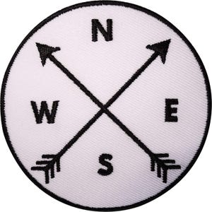 May include: A circular embroidered patch featuring a white background with a black border. The design includes two crossed black arrows and the black embroidered letters N, E, W, and S positioned at the top, right, left, and bottom respectively.