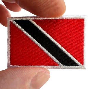 May include: A rectangular embroidered patch featuring the national flag of Trinidad and Tobago. The design consists of a red field divided by a diagonal black stripe running from the upper left to the lower right, bordered by two thin white stripes.