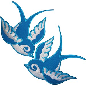 Puede incluir: Dos parches bordados de golondrinas con cuerpo azul vibrante y detalles de alas en blanco. Cada ave se muestra en posición de vuelo con las alas extendidas, exhibiendo un diseño estilizado con costuras limpias y contornos bien definidos.