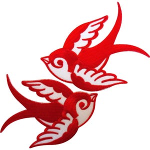 Puede incluir: Dos parches bordados de golondrinas con un diseño en colores rojo y blanco vibrantes. Cada ave se muestra en una pose de vuelo estilizada con las alas extendidas, destacando costuras detalladas que definen las plumas y el cuerpo.