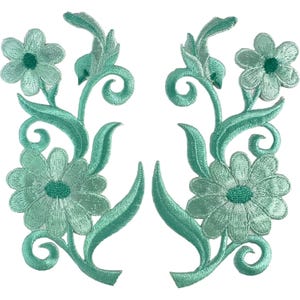 May include: A pair of matching mint green embroidered floral patches featuring two distinct blossoms, swirling vine accents, and pointed leaves. The embroidery displays a light mint green thread with darker green centres on each flower, creating a symmetrical design.