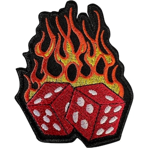 May include: An embroidered patch featuring two red dice with white pips positioned in front of stylised yellow and orange flames. The entire design is outlined with a thick black border, creating a high-contrast graphic suitable for fabric application.