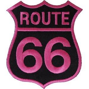 May include: A shield-shaped embroidered patch featuring a black background with a vibrant pink border. The text ROUTE is stitched in pink at the top, and the number 66 is prominently displayed in large pink characters in the center of the patch.
