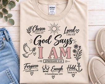 May include: A beige crew neck t-shirt featuring black and light pink graphic text that reads God Says I AM. The design includes illustrations of a sun, a dove, a flower, a crown, and an anchor, along with various Bible verse references.
