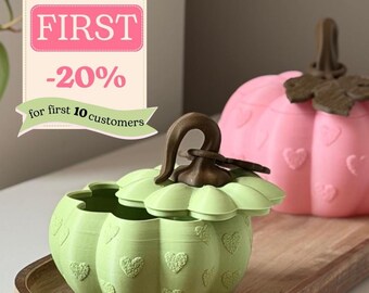 May include: A light green pumpkin-shaped container with a brown stem and lid, featuring embossed heart patterns. A second pink pumpkin container with a brown stem and heart details is visible behind it. A banner displays the text With code FIRST -20% for first 10 customers.