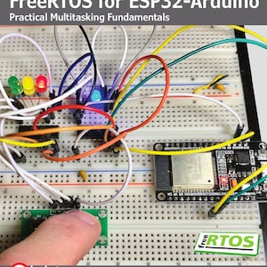 May include: A white breadboard with an ESP32-Arduino microcontroller, colorful jumper wires, and three LEDs. The text reads FreeRTOS for ESP32-Arduino Practical Multitasking Fundamentals, elektor, and Warren Gay. A finger presses a small green module.