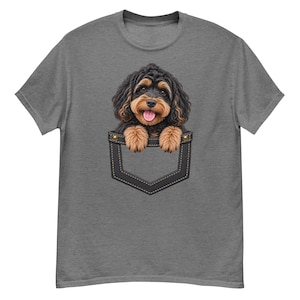 Peut inclure: Un t-shirt gris chiné à manches courtes orné d'un motif représentant un chiot aux poils bouclés noirs et feu qui sort d'une fausse poche de poitrine gris foncé. Le chiot a des oreilles tombantes, un museau marron et la langue tirée.