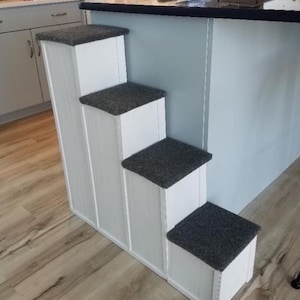 May include: White wooden pet steps with gray carpet treads. The steps are attached to a white kitchen island.