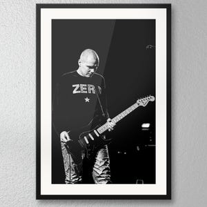 May include: A black and white framed photograph of a bald musician playing an electric guitar. The musician wears a long-sleeved shirt with the word ZERO and a star printed on the chest. The guitar has a light-colored neck and a dark body.