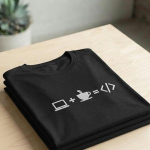 May include: A black t-shirt featuring a white embroidered graphic of a laptop, a plus sign, a steaming coffee cup, an equals sign, and code brackets. The design represents the equation of laptop plus coffee equals code, centered on the chest.