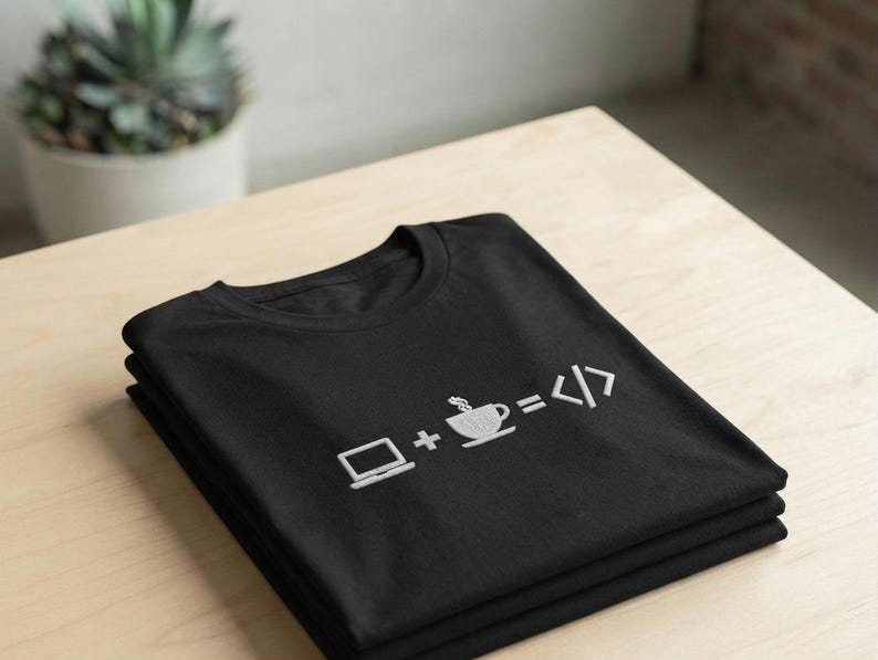 May include: A black t-shirt featuring a white embroidered graphic of a laptop, a plus sign, a steaming coffee cup, an equals sign, and code brackets. The design represents the equation of laptop plus coffee equals code, centered on the chest.