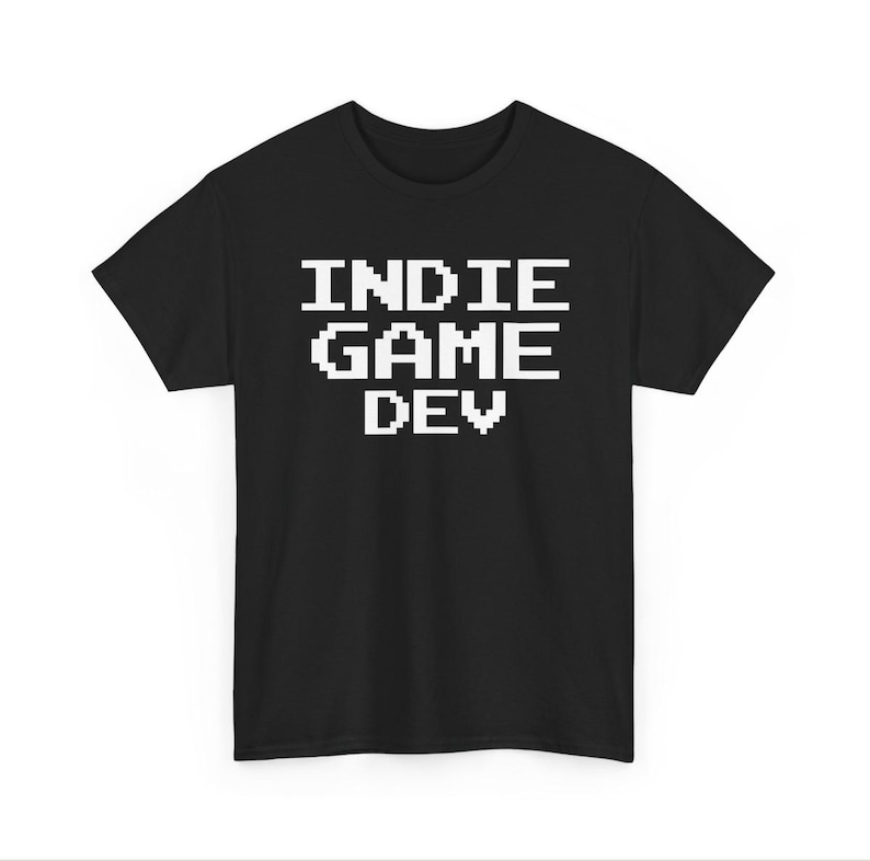 May include: A black short-sleeved t-shirt featuring the white pixelated text INDIE GAME DEV centered on the chest. The garment has a crew neckline and a standard fit, showcasing a clean design with bold, blocky lettering in a retro video game style.