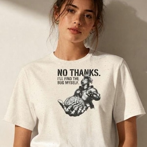 Op de afbeelding: Een gespikkeld gebroken wit t-shirt met een zwarte afbeelding van een ridder in harnas die een menselijk brein vasthoudt. Boven de illustratie staat de tekst: NO THANKS. I'LL FIND THE BUG MYSELF. Het t-shirt heeft korte mouwen en een ronde hals.