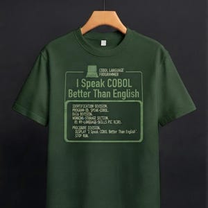 Puede incluir: Una camiseta de manga corta de color verde oscuro con un icono de ordenador y el texto: COBOL LANGUAGE PROGRAMMER, I Speak COBOL Better Than English, IDENTIFICATION DIVISION, PROGRAM-ID, DATA DIVISION, WORKING-STORAGE SECTION, PROCEDURE DIVISION.
