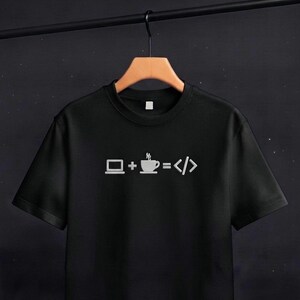 May include: A black short-sleeved t-shirt featuring a white graphic print on the chest. The design displays a laptop icon, a plus sign, a steaming coffee cup icon, an equals sign, and code brackets, representing the equation laptop plus coffee equals code.
