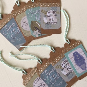 May include: Six brown gift tags with twine, featuring various designs and text. The tags have a blue and white color scheme with a nautical theme. The text on the tags includes "Time Tid", "Think Happy Be Happy", "Saw Life", and "Always We Go".
