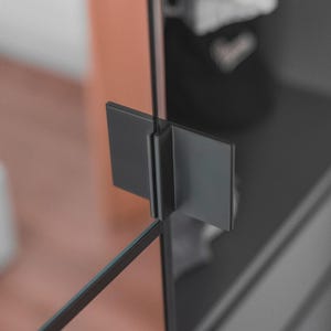 May include: A matte black metal glass door hinge featuring a rectangular plate design. The hinge is mounted on a vertical glass panel, providing a secure connection between two glass surfaces with a clean, industrial aesthetic and smooth finish.