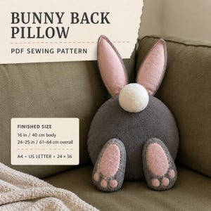 May include: A PDF sewing pattern for a bunny back pillow. The design features a round dark gray body, two long pink and gray ears, a white pom-pom tail, and two gray feet with pink pads. Finished body size is 16 inches, with 24-25 inches overall.