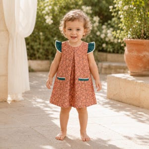 May include: A sleeveless dress featuring a rust-coloured floral pattern with dark teal ruffled cap sleeves and two front pockets accented with white trim. The dress has a round neckline and a pleated front design, falling to a knee-length hemline.