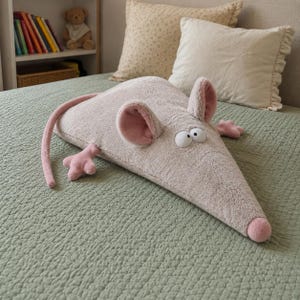Puede incluir: Un juguete de peluche con forma de ratón en color beige claro con una textura suave y difusa. Presenta orejas grandes y redondeadas con detalles interiores en rosa, dos ojos blancos anchos con pupilas negras, una pequeña nariz rosa, cuatro extremidades rosas y una cola rosa larga y fina.