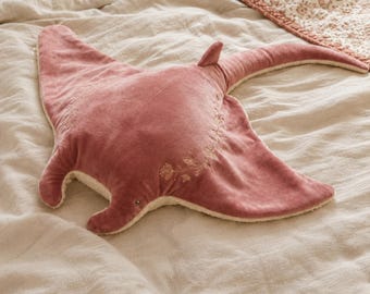 May include: A plush stingray-shaped pillow in a dusty rose velvet fabric. The top surface features delicate, light-colored floral embroidery along the center and wings. The underside and edges are lined with a soft, cream-colored textured material.