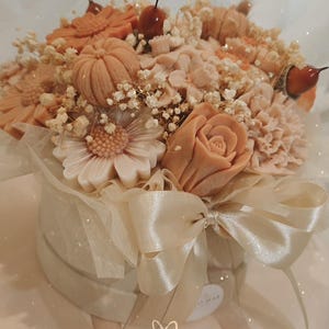 Op de afbeelding: Een ronde geschenkdoos versierd met een crèmekleurig lint en strik, gevuld met een arrangement van perzik- en oranjegekleurde bloem- en pompoenvormige items, geaccentueerd met kleine witte droogbloemen en de tekst beautiful met een hartje.