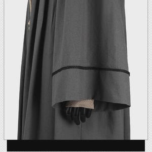 May include: A dark gray robe featuring long, wide sleeves with a black braided trim detail around the cuffs. The garment has a structured, pleated design with a vertical black braided trim running along the side of the main body fabric.