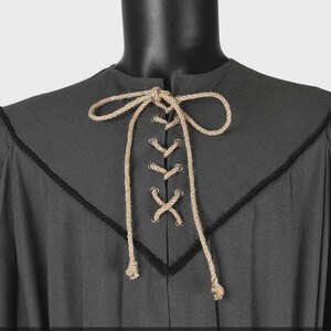 May include: A dark gray tunic featuring a V-shaped neckline accented with black trim. The front closure includes silver-toned metal grommets laced with a thick, natural-colored jute rope that is tied into a bow at the top center of the chest.
