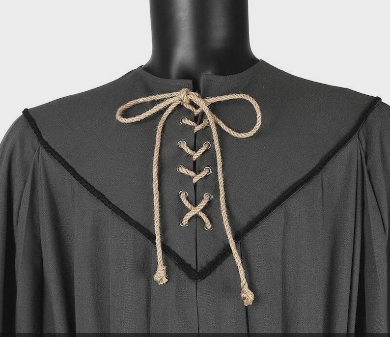 May include: A dark gray tunic featuring a V-shaped neckline accented with black trim. The front closure includes silver-toned metal grommets laced with a thick, natural-colored jute rope that is tied into a bow at the top center of the chest.