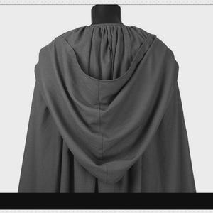 May include: A dark gray hooded cloak featuring a gathered neckline and a deep, draped hood. The garment is constructed from a solid-colored fabric with a visible texture, hanging in vertical folds from the shoulders down to the hemline.