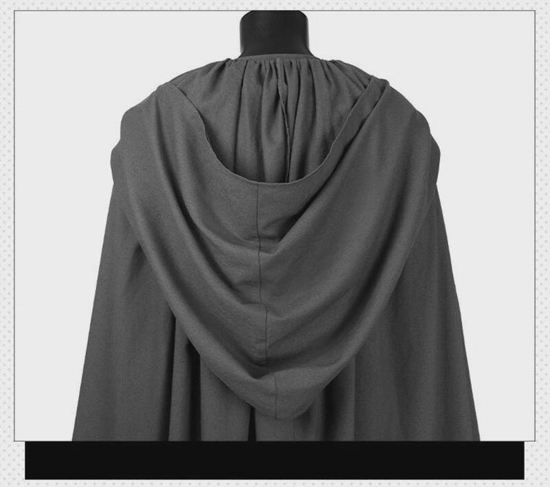 May include: A dark gray hooded cloak featuring a gathered neckline and a deep, draped hood. The garment is constructed from a solid-colored fabric with a visible texture, hanging in vertical folds from the shoulders down to the hemline.