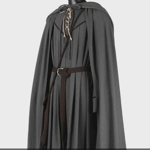 May include: A dark gray hooded cloak worn over a matching pleated tunic. The tunic features a lace-up neckline with light-colored cords and a dark brown woven belt with a metal buckle cinched at the waist, completing the layered ensemble.