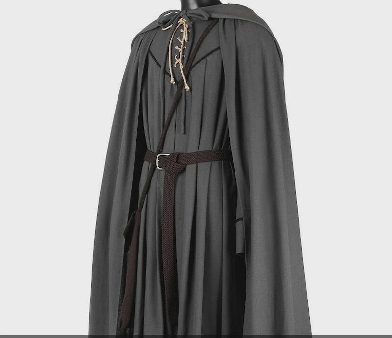 May include: A dark gray hooded cloak worn over a matching pleated tunic. The tunic features a lace-up neckline with light-colored cords and a dark brown woven belt with a metal buckle cinched at the waist, completing the layered ensemble.