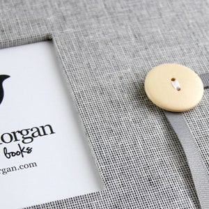 Może przedstawiać: Szary, lniany album na wspomnienia z białym zapięciem na guzik i logo z napisem "Good Morgan memory books good-morgan.com"
