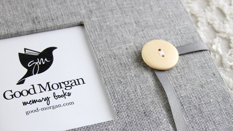 Może przedstawiać: Szary, lniany album na wspomnienia z białym zapięciem na guzik i logo z napisem "Good Morgan memory books good-morgan.com"