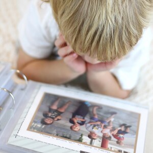 May include: A child looking at a photo album with pictures of children in it. The photo album is open to a page with a photo of four children.