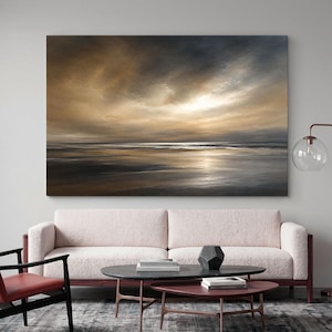 Può includere: Una grande stampa artistica da parete rettangolare con un dipinto a olio di un paesaggio costiero al tramonto. La scena raffigura un cielo scuro e nuvoloso con luce dorata che filtra sopra un oceano calmo e una riva sabbiosa.