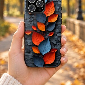 May include: A smartphone case featuring a dark gray textured brick background adorned with a vertical arrangement of vibrant orange and deep blue leaves. The design includes a prominent camera cutout at the top left corner of the rectangular case.