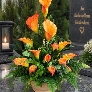 Pode incluir: Um arranjo floral com vários lírios-de-água cor de laranja e folhagem verde num vaso redondo. As flores estão dispostas numa exibição vertical com alturas variadas, rodeadas por pequenas folhas verdes e ramos semelhantes a fetos.