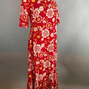 May include: A red dress with a floral print, short sleeves, and a ruffled hem. The dress has a pattern of white and yellow flowers on a red background. The dress is displayed on a mannequin.
