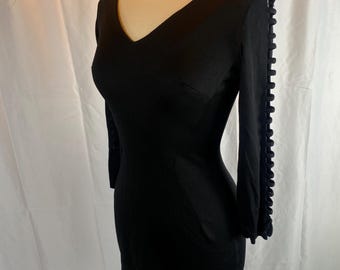 May include: A black mini dress with a v-neck and three-quarter sleeves. The sleeves have a decorative detail of braided fabric.