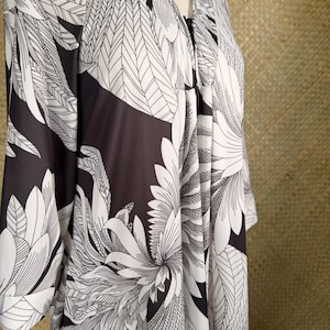 May include: A long-sleeved robe featuring a high-contrast black and white graphic print of large, stylized feathers or leaves. The garment has a V-neckline, a front opening, and a flowing silhouette with gathered fabric details at the shoulder area.