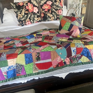 May include: A colorful patchwork quilt and matching pillow set on a bed. The quilt features a variety of fabric pieces in red, blue, green, and other colors. Two pillows with a floral pattern and one patchwork pillow complete the bedding.