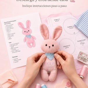 Puede incluir: Un juguete de conejo de peluche rosa con un pañuelo de cuello a rayas azules y blancas, acompañado de hojas de patrones de costura impresas tituladas Moldes PDF, carretes de hilo rosa y azul, y platos blancos con alfileres y retazos.